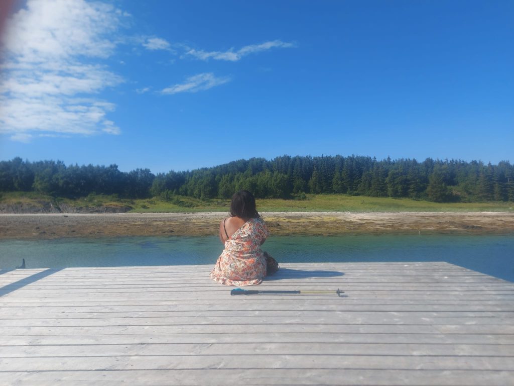 Femme assise sur pont en bois, regarde l'horizon.