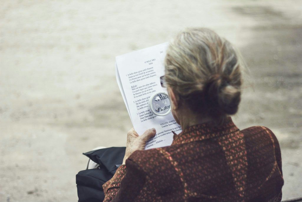 Dame âgée qui lit un texte à l'aide d'une loupe